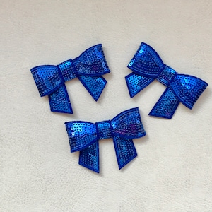 Puede incluir: Tres adornos de lazo de lentejuelas azules. Cada lazo está hecho de lentejuelas azules y tiene una forma de lazo clásica.