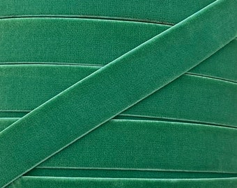May include: Close-up of a green velvet ribbon. The ribbon is folded in a criss-cross pattern, showing the soft texture of the fabric.