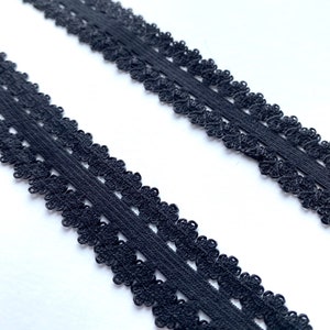 May include: Two strips of black lace trim with a scalloped floral design. The trim is made of a soft, flexible material and is suitable for various sewing and craft projects. The lace is set against a white background.