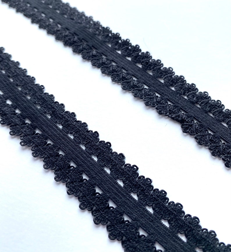 May include: Two strips of black lace trim with a scalloped floral design. The trim is made of a soft, flexible material and is suitable for various sewing and craft projects. The lace is set against a white background.