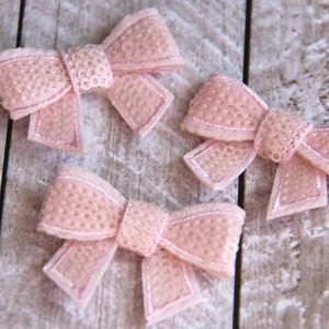 May include: Three pink fabric bows with a sparkly texture. The bows are on a wooden surface.