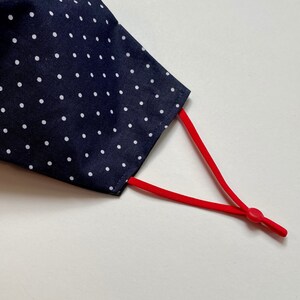 May include: A navy blue face mask with white polka dots and red adjustable ear loops.