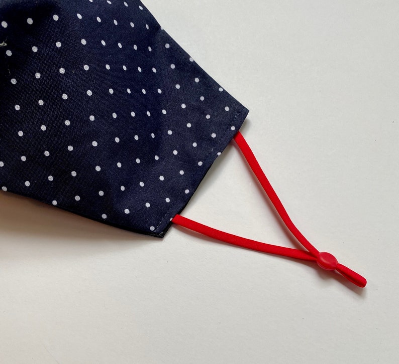 May include: A navy blue face mask with white polka dots and red adjustable ear loops.