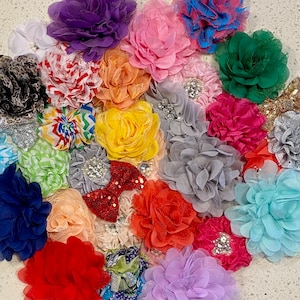 May include: A collection of colorful fabric flowers in various shapes and sizes. The flowers are made of different materials, including lace, satin, and chiffon. They are arranged in a random pattern on a white background.