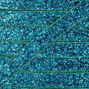 May include: Close-up of turquoise blue glitter ribbon. The ribbon is made of a soft, velvety material and is covered in sparkling glitter.