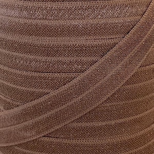Puede incluir: Primer plano de tela elástica marrón con textura acanalada. La tela está doblada y superpuesta, mostrando la textura y la forma en que se estira.
