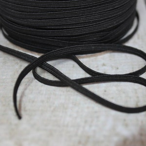 May include: A spool of black elastic cord, with a length of the cord lying on a wooden surface.
