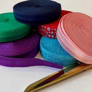 May include: Assortment of colorful elastic ribbon rolls in green, purple, pink, blue, and navy blue. A gold ruler and gold scissors are also included.