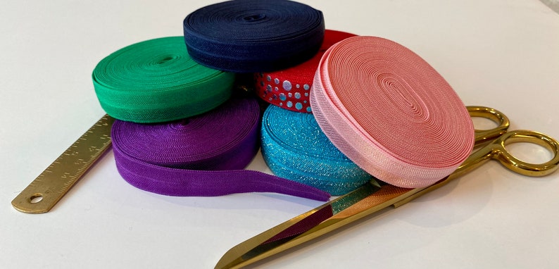 May include: Assortment of colorful elastic ribbon rolls in green, purple, pink, blue, and navy blue. A gold ruler and gold scissors are also included.
