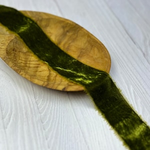 May include: A dark green velvet ribbon with frayed edges is displayed on a wooden bowl. The ribbon is soft and luxurious, perfect for adding a touch of elegance to any project.