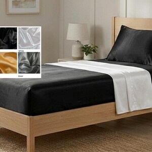 May include: A bed with a wooden frame featuring black satin sheets and a black satin pillowcase, with a white flat sheet draped across the center. An inset grid displays six color options: hot pink, black, white, ivory, gold, and silver.