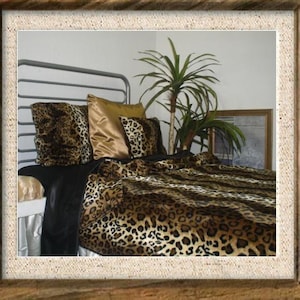 May include: A bed with a metal frame is adorned with leopard print bedding, including a comforter and matching pillows. A gold satin pillow adds a touch of luxury. A black sheet and a decorative plant complete the bedroom scene.