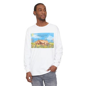 May include: White long-sleeve shirt with a colorful graphic of a sleeping orange tabby cat in a field with text that reads "But today human, I'm on my month nap, just dreaming about how lucky you are to have me."