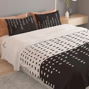 Könnte beinhalten: Ein Bett mit einer weißen Bettdecke und zwei schwarzen Kissenbezügen. Die Kissenbezüge haben ein weißes Strichmuster. Die Bettdecke hat ein schwarz-weißes Strichmuster. Zwei beige Kissen befinden sich hinter den schwarzen Kissenbezügen.