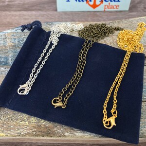 May include: Three different chain necklaces in silver, gold, and bronze colours. The chains are displayed on a dark blue velvet pouch.