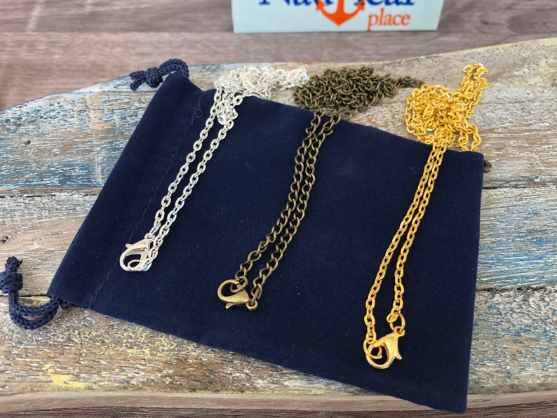May include: Three different chain necklaces in silver, gold, and bronze colours. The chains are displayed on a dark blue velvet pouch.