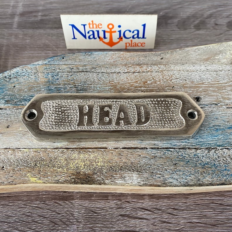 May include: A silver metal sign with the word "HEAD" embossed on it. The sign is mounted on a weathered wooden surface.