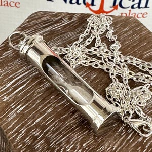 May include: A silver chain necklace with a silver hourglass pendant. The hourglass is filled with white sand and has a clear glass tube.