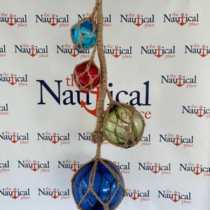 May include: A set of four nautical buoy floats hanging from a rope. The floats are blue, red, green, and white with a brown rope net around each one.