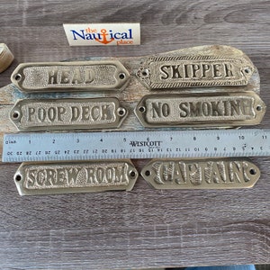 May include: Six brass plaques with nautical themed words, including "Head", "Skipper", "Poop Deck", "No Smoking", "Screw Room", and "Captain".