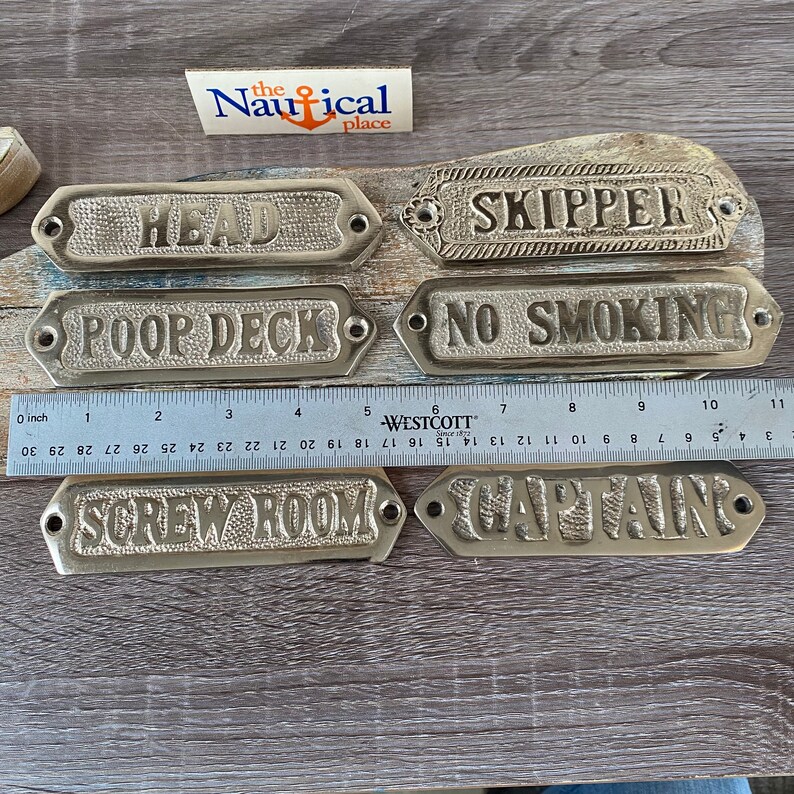 May include: Six brass plaques with nautical themed words, including "Head", "Skipper", "Poop Deck", "No Smoking", "Screw Room", and "Captain".
