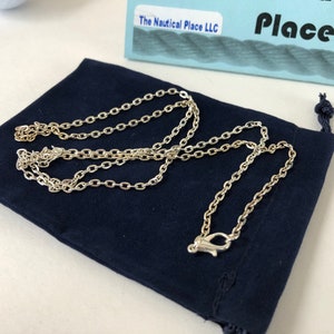 Pu&ograve; includere: Una collana a catena d'argento con una chiusura a moschettone, esposta in una pochette di velluto blu scuro. La pochette ha una chiusura con coulisse ed &egrave; etichettata "The Nautical Place LLC".