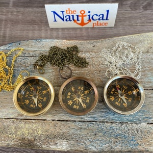 May include: Three antique-style compass necklaces with gold, silver, and bronze chains. Each compass has a black face with gold markings and a gold needle.