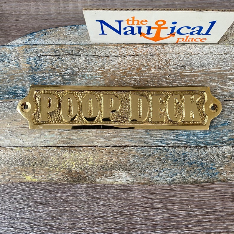 May include: A brass sign with the words "POOP DECK" embossed on it. The sign has rounded corners and two small holes on either side for hanging.