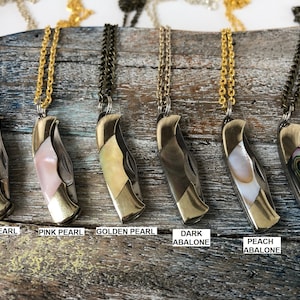 Pu&ograve; includere: Sei collane diverse con un coltellino tascabile e diverse intarsi di conchiglia. Le collane sono in ottone e hanno una catena dorata. Gli intarsi di conchiglia sono in madreperla bianca, madreperla rosa, madreperla dorata, abalone scuro, abalone pesca e abalone.