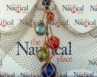 May include: A decorative hanging cluster of six spherical glass fishing floats in various colors including dark blue, orange, light blue, red, and green. Each glass sphere is encased in a hand-knotted tan jute rope netting, suspended together.