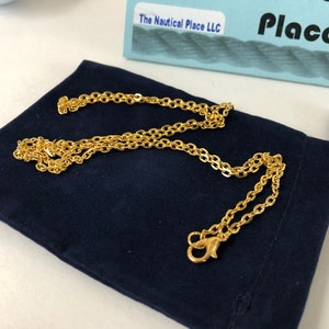 Pu&ograve; includere: Una collana a catena dorata con chiusura a moschettone, presentata in una pochette di velluto blu scuro. La catena &egrave; composta da piccole forme ovali collegate.