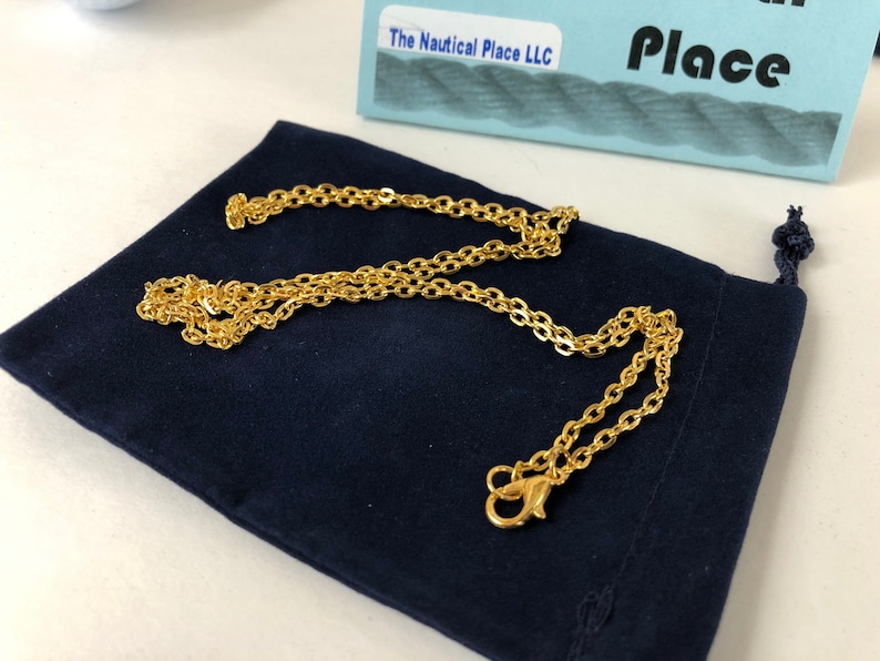 Pu&ograve; includere: Una collana a catena dorata con chiusura a moschettone, presentata in una pochette di velluto blu scuro. La catena &egrave; composta da piccole forme ovali collegate.