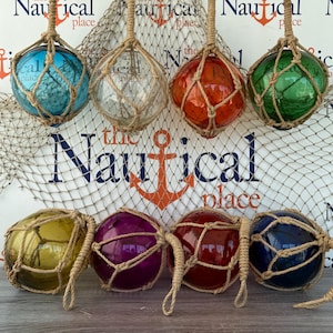 May include: Eight spherical glass floats in blue, clear, orange, green, yellow, purple, red, and dark blue, each encased in a decorative tan rope netting. The floats are arranged in two rows against a background with a fishing net and text.