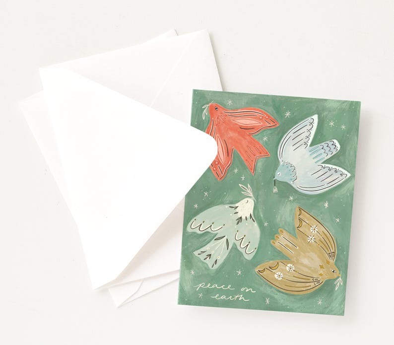 Pu&ograve; includere: Un biglietto di auguri con quattro colombe illustrate in rosso, blu e oro su sfondo verde. Il biglietto recita "peace on earth". Buste bianche sono visibili accanto al biglietto.