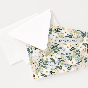 Op de afbeelding: Twee witte enveloppen en twee baby shower wenskaarten. De kaarten hebben een lichtblauwe achtergrond met een bloemenpatroon van witte, oranje en blauwe bloemen en groene bladeren. De woorden "welcome baby" staan op de kaarten.