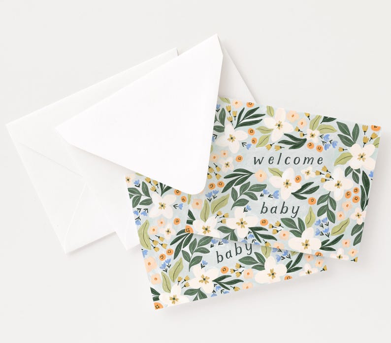 Op de afbeelding: Twee witte enveloppen en twee baby shower wenskaarten. De kaarten hebben een lichtblauwe achtergrond met een bloemenpatroon van witte, oranje en blauwe bloemen en groene bladeren. De woorden "welcome baby" staan op de kaarten.