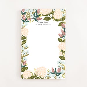 Op de afbeelding: Blok met bloemenmotief met een witte achtergrond en een rand van roze, witte en blauwe bloemen. De tekst "a note from MILLIE WALLACE" staat bovenaan het blok gedrukt.