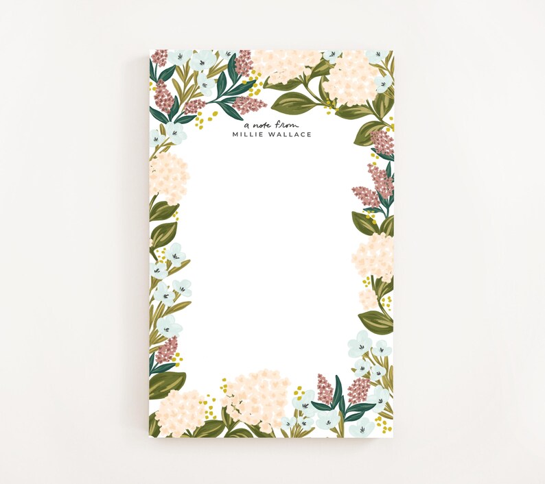 Op de afbeelding: Blok met bloemenmotief met een witte achtergrond en een rand van roze, witte en blauwe bloemen. De tekst "a note from MILLIE WALLACE" staat bovenaan het blok gedrukt.