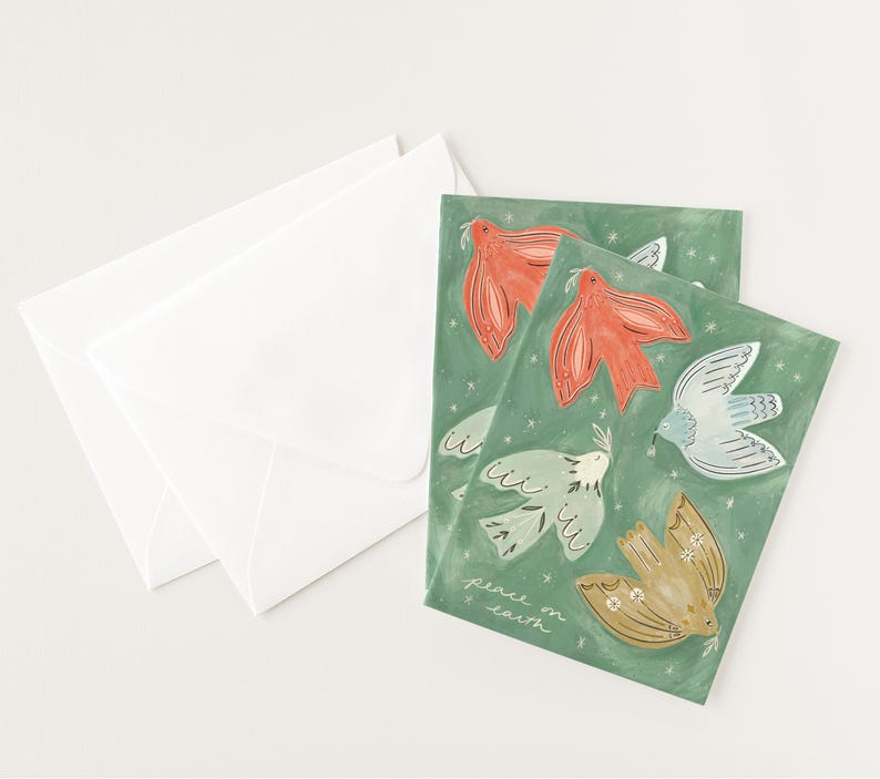 Pu&ograve; includere: Biglietti di auguri con illustrazioni di colombe rosse, blu e oro su sfondo verde. I biglietti sono accompagnati da buste bianche. La frase "peace on earth" &egrave; scritta sulla carta.