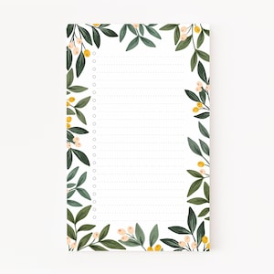 Puede incluir: Un bloc de notas blanco con un borde floral. El borde presenta hojas verdes, bayas blancas y flores amarillas. El bloc de notas tiene papel rayado y un agujero perforado en la parte superior.