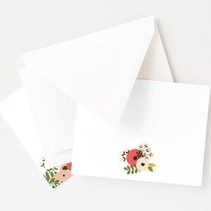 May include: A set of white note cards with a floral design in shades of pink, red, and green. The floral design features a cluster of flowers with a white center and pink and red petals.