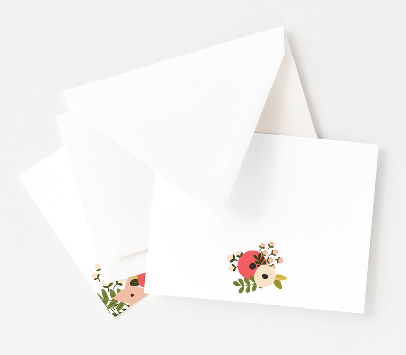 May include: A set of white note cards with a floral design in shades of pink, red, and green. The floral design features a cluster of flowers with a white center and pink and red petals.