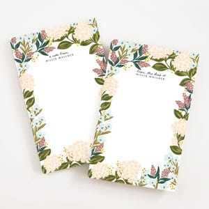 Op de afbeelding: Twee blokken met bloemenmotief met een witte achtergrond en een rand van roze, blauwe en groene bloemen. De bovenste blocnote zegt "a note from Millie Wallace" en de onderste blocnote zegt "from the desk of Millie Wallace".