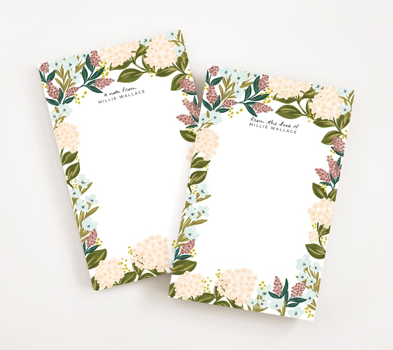 Op de afbeelding: Twee blokken met bloemenmotief met een witte achtergrond en een rand van roze, blauwe en groene bloemen. De bovenste blocnote zegt "a note from Millie Wallace" en de onderste blocnote zegt "from the desk of Millie Wallace".