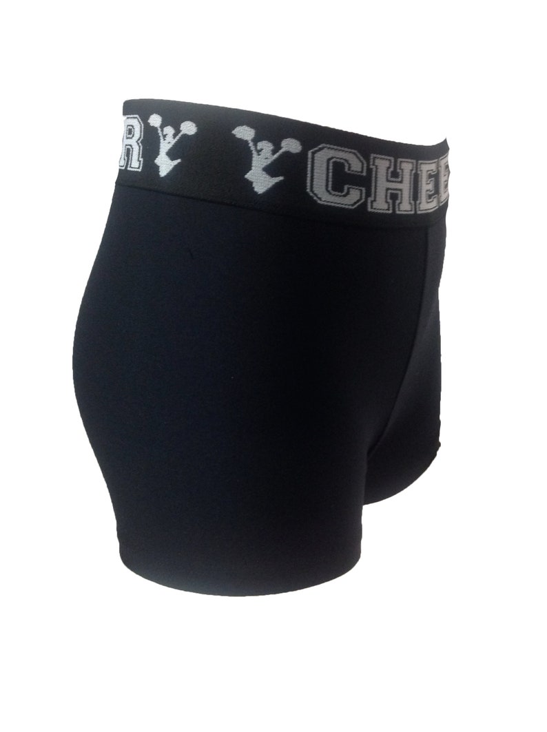 May include: Black athletic shorts with a white waistband. The waistband features the text "VERY CHEER" in white block letters with a cheerleader graphic. The shorts are made of a stretchy material.