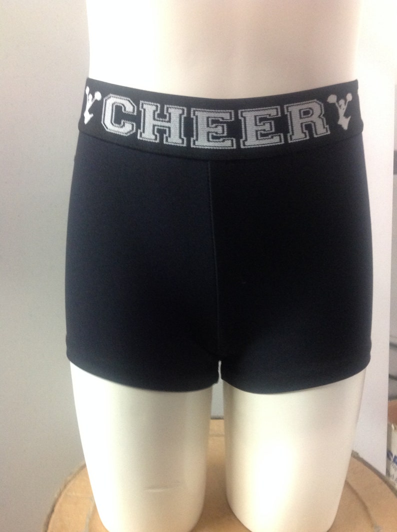 May include: Black athletic shorts with a white waistband featuring the word "CHEER" in a block letter design. The shorts are displayed on a mannequin.