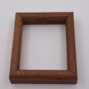 May include: A rectangular, empty wooden picture frame with a warm brown finish. The frame has a simple, classic design with a visible wood grain texture. It is designed to hold a photograph or artwork and is ready to be hung.