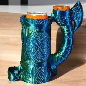 Op de afbeelding: Een blauwe en groene 3D-geprinte mok met een bijlhandvat en een blikhouder. De mok heeft een gedetailleerd ontwerp met een schild en een bladpatroon. De mok staat op een houten oppervlak.