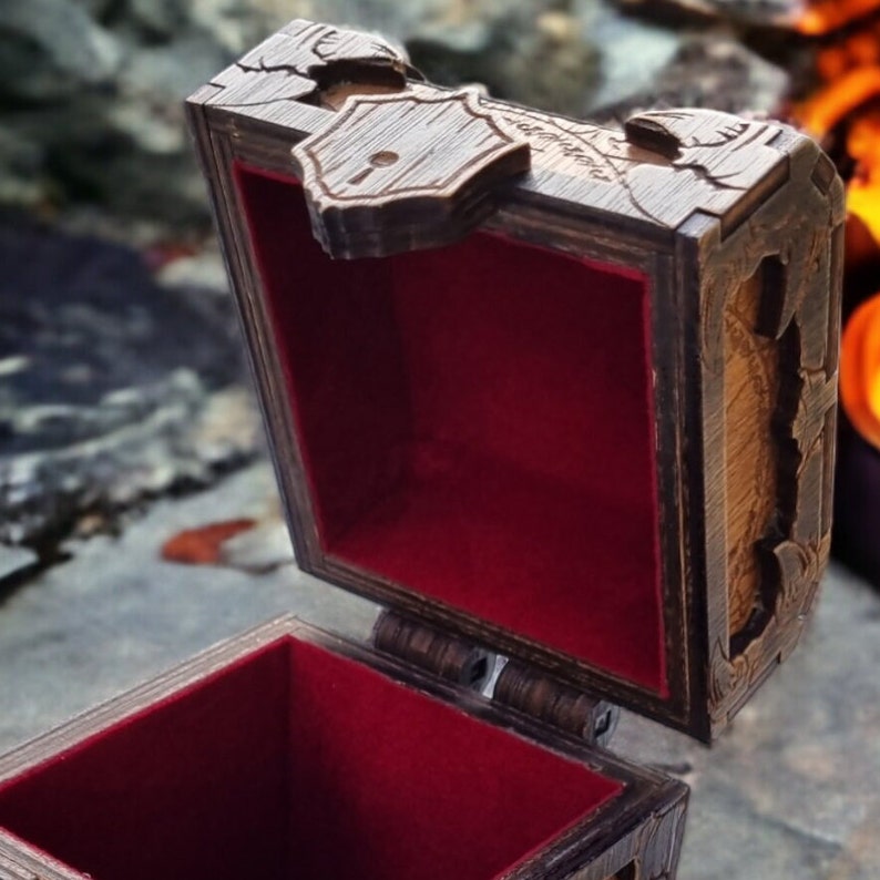 May include: Wooden treasure chest with a hinged lid, open to reveal a red velvet interior. The chest has intricate carved details and a decorative lock. The exterior is a dark brown color, with a distressed finish.