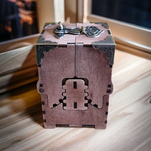 May include: A wooden box with a hinged lid and intricate metal hardware. The box is a warm brown color, with decorative corner accents and a clasp. The design features a unique interlocking mechanism on the front.